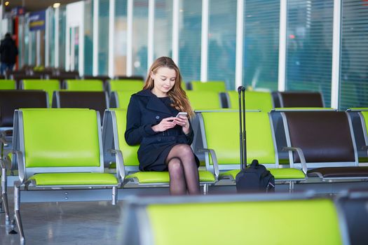Young woman in international airport, checking her phone while waiting for her flight