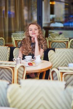 Beautiful Parisian woman in cafe, drinking coffee and eating macaroons, traditional French dessert