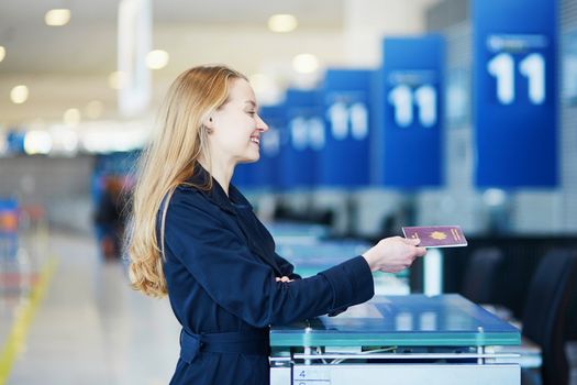 Young woman in international airport at check-in counter, giving her passport to an officer and waiting for her boarding pass