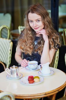 Beautiful Parisian woman in cafe, drinking coffee and eating macaroons, traditional French dessert