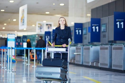 Young woman in international airport, with luggage trolley
