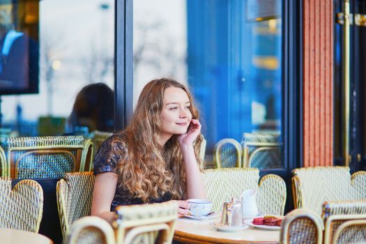 Beautiful Parisian woman in cafe, drinking coffee and eating macaroons, traditional French dessert