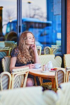 Beautiful Parisian woman in cafe, drinking coffee and eating macaroons, traditional French dessert