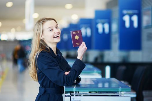 Young woman in international airport at check-in counter, giving her passport to an officer and waiting for her boarding pass