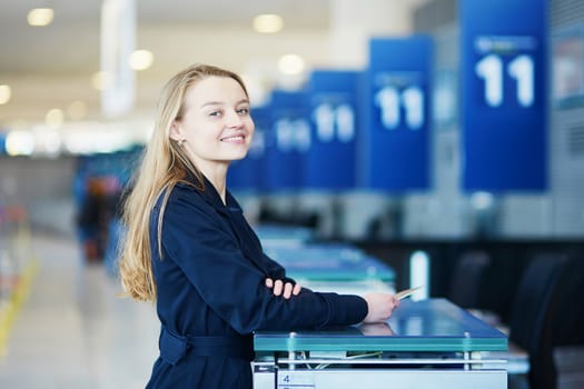 Young woman in international airport at check-in counter, giving her passport to an officer and waiting for her boarding pass