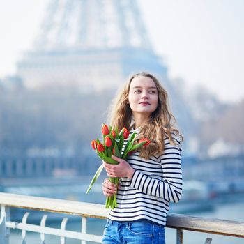 Beautiful young girl with bunch of red tulips near the Eiffel tower in Paris, France on a clear spring day