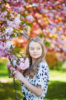 Beautiful young woman enjoying sunny day in park during cherry blossom season on a nice spring day