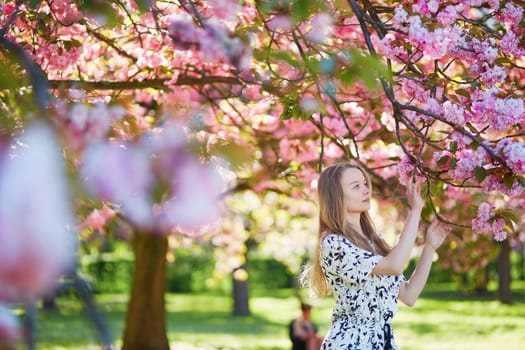 Beautiful young woman enjoying sunny day in park during cherry blossom season on a nice spring day