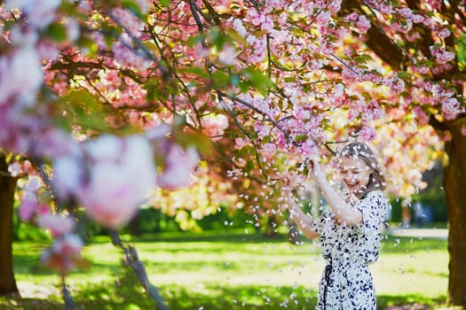 Beautiful young woman enjoying sunny day in park during cherry blossom season on a nice spring day