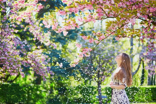 Beautiful young woman enjoying sunny day in park during cherry blossom season on a nice spring day