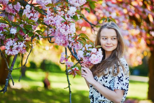 Beautiful young woman enjoying sunny day in park during cherry blossom season on a nice spring day