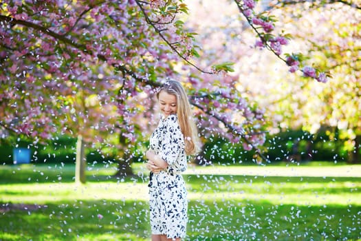 Beautiful young woman enjoying sunny day in park during cherry blossom season on a nice spring day