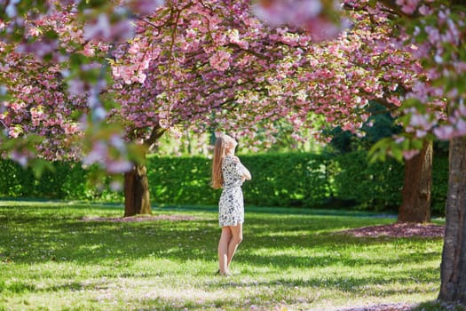 Beautiful young woman enjoying sunny day in park during cherry blossom season on a nice spring day