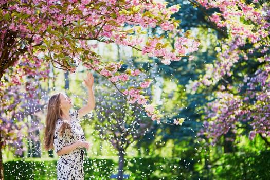 Beautiful young woman enjoying sunny day in park during cherry blossom season on a nice spring day