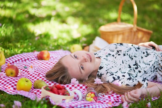Beautiful young woman having picnic in parc, lying on her back with fruits around her