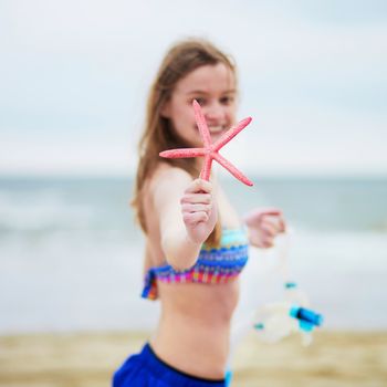 Happy young woman in bikini with snorkelling equipment and pink starfish enjoying summer vacation holidays by ocean or sea. Beach, travelling and people concept