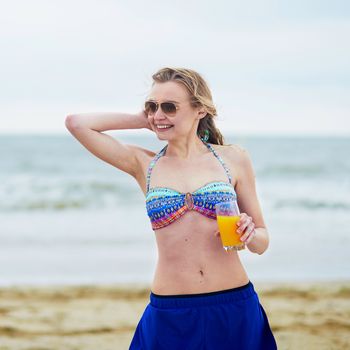 Beautiful young woman relaxing and sunbathing on beach, drinking delicious fruit juice