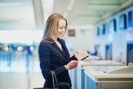 Young business woman in international airport at check-in counter, giving her passport to an officer and waiting for her boarding pass