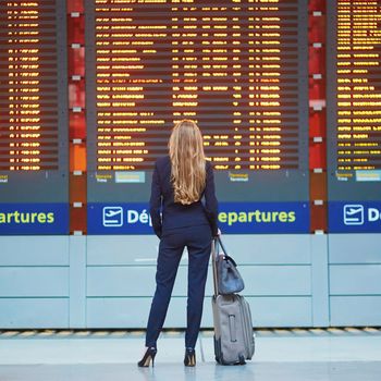 Young woman in international airport near large information display