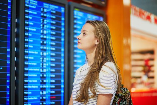 Young woman in international airport looking at the flight information board, checking her flight