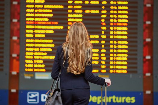 Young woman in international airport near large information display