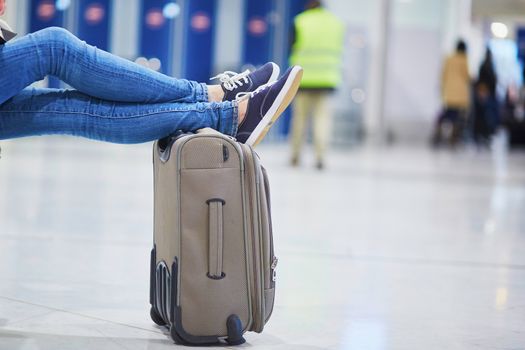 Closeup of woman feet on a suitcase in international airport. Delayed or canceled flight concept