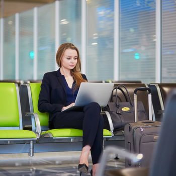 Young woman in international airport working on laptop while waiting for her flight