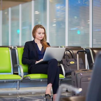 Young woman in international airport working on laptop while waiting for her flight