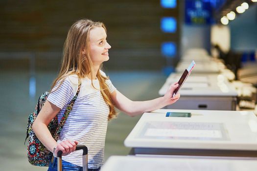 Beautiful young tourist girl with backpack and carry on luggage in international airport at check-in counter, giving her passport to an officer and waiting for her boarding pass