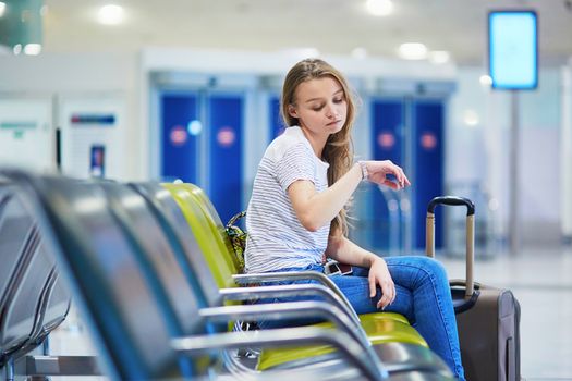 Beautiful young tourist girl with backpack and carry on luggage in international airport, waiting for her flight, looking worried. Delayed or canceled flight concept