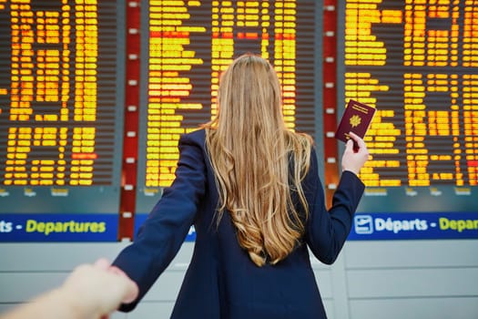 Young woman in international airport near large information display, follow me concept