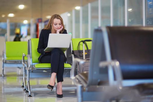 Young woman in international airport working on laptop while waiting for her flight