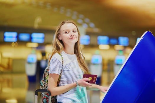 Beautiful young tourist girl with backpack and carry on luggage in international airport, doing self check-in