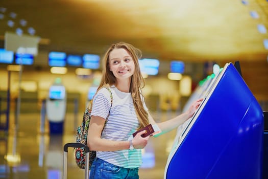 Beautiful young tourist girl with backpack and carry on luggage in international airport, doing self check-in