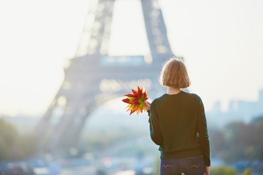 Beautiful young French woman with bunch of colorful autumn leaves near the Eiffel tower in Paris on a fall day