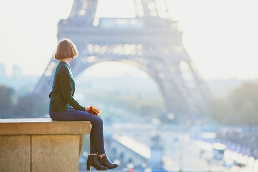 Beautiful young French woman with bunch of colorful autumn leaves near the Eiffel tower in Paris on a fall day