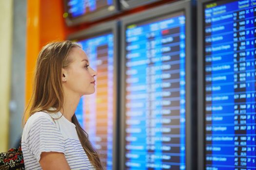 Young woman in international airport looking at the flight information board, checking her flight