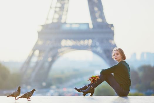 Beautiful young French woman with bunch of colorful autumn leaves near the Eiffel tower in Paris on a fall day