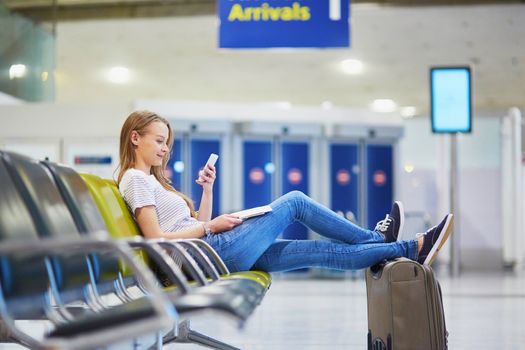 Young woman in international airport reading a book while waiting for her flight