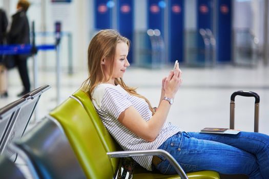 Young woman in international airport using mobile phone while waiting for her flight