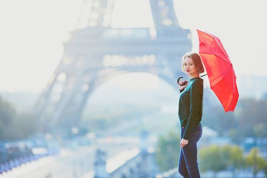Beautiful young girl with red umbrella in Paris near the Eiffel tower at morning