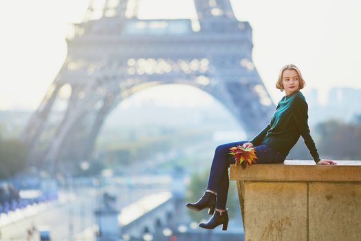 Beautiful young French woman with bunch of colorful autumn leaves near the Eiffel tower in Paris on a fall day