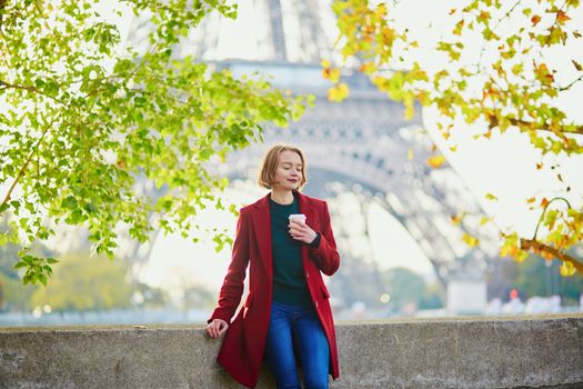 Beautiful young French woman drinking coffee near the Eiffel tower in Paris on a fall or spring day