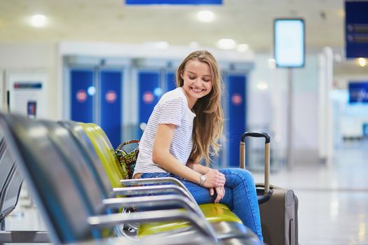 Beautiful young tourist girl with backpack and carry on luggage in international airport, waiting for flight