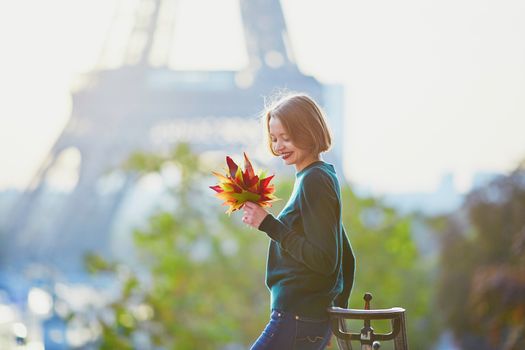 Beautiful young French woman with bunch of colorful autumn leaves near the Eiffel tower in Paris on a fall day
