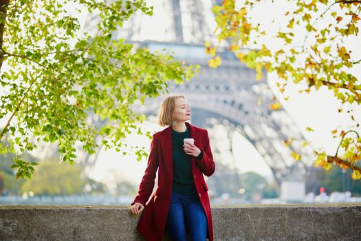 Beautiful young French woman with bunch of colorful autumn leaves near the Eiffel tower in Paris on a fall day