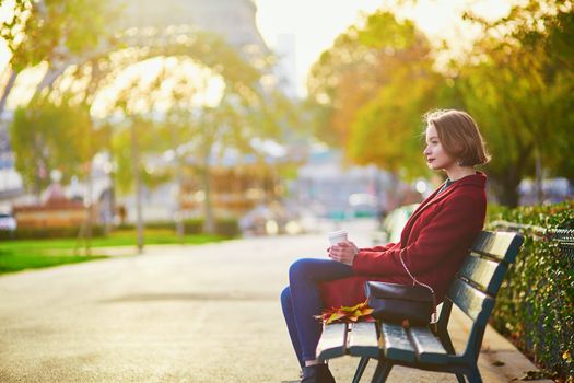 Beautiful young French woman with bunch of colorful autumn leaves sitting on the bench near the Eiffel tower in Paris on a fall day