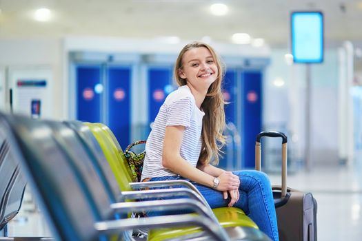 Beautiful young tourist girl with backpack and carry on luggage in international airport, waiting for flight