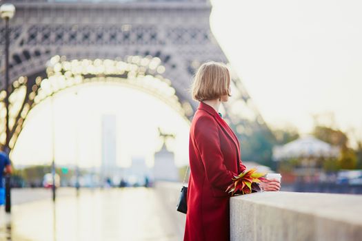 Beautiful young French woman drinking coffee near the Eiffel tower in Paris on a fall or spring day