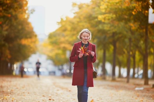 Beautiful young woman with bunch of colorful autumn leaves walking in park on a fall day